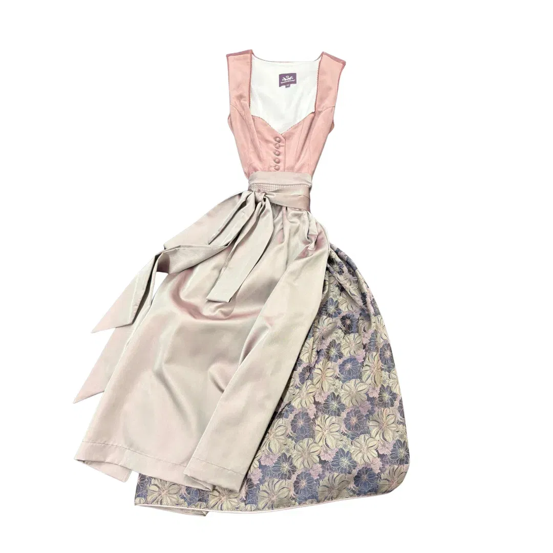 Ein traditionelles Dirndlkleid mit blassrosa Mieder, passender Schärpe und einem Rock mit Blumenmuster in Lila-, Grün- und Cremetönen, flach auf weißem Grund.