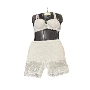 Eine schwarze Schaufensterpuppe, die ein passendes Dessous-Set aus weißer Spitze, darunter einen BH und Shorts mit hoher Taille und Wellenschliff, vor einem schlichten weißen Hintergrund präsentiert.